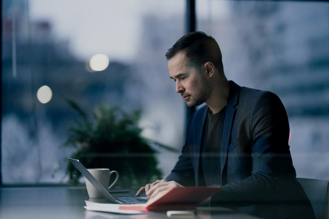 A man sits at a desk typing on a laptop