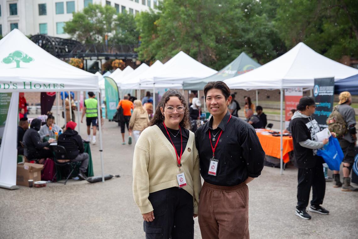 Hanna Woodward and Bill Zheng stand in front of booths at the Pop-Up Care Village.